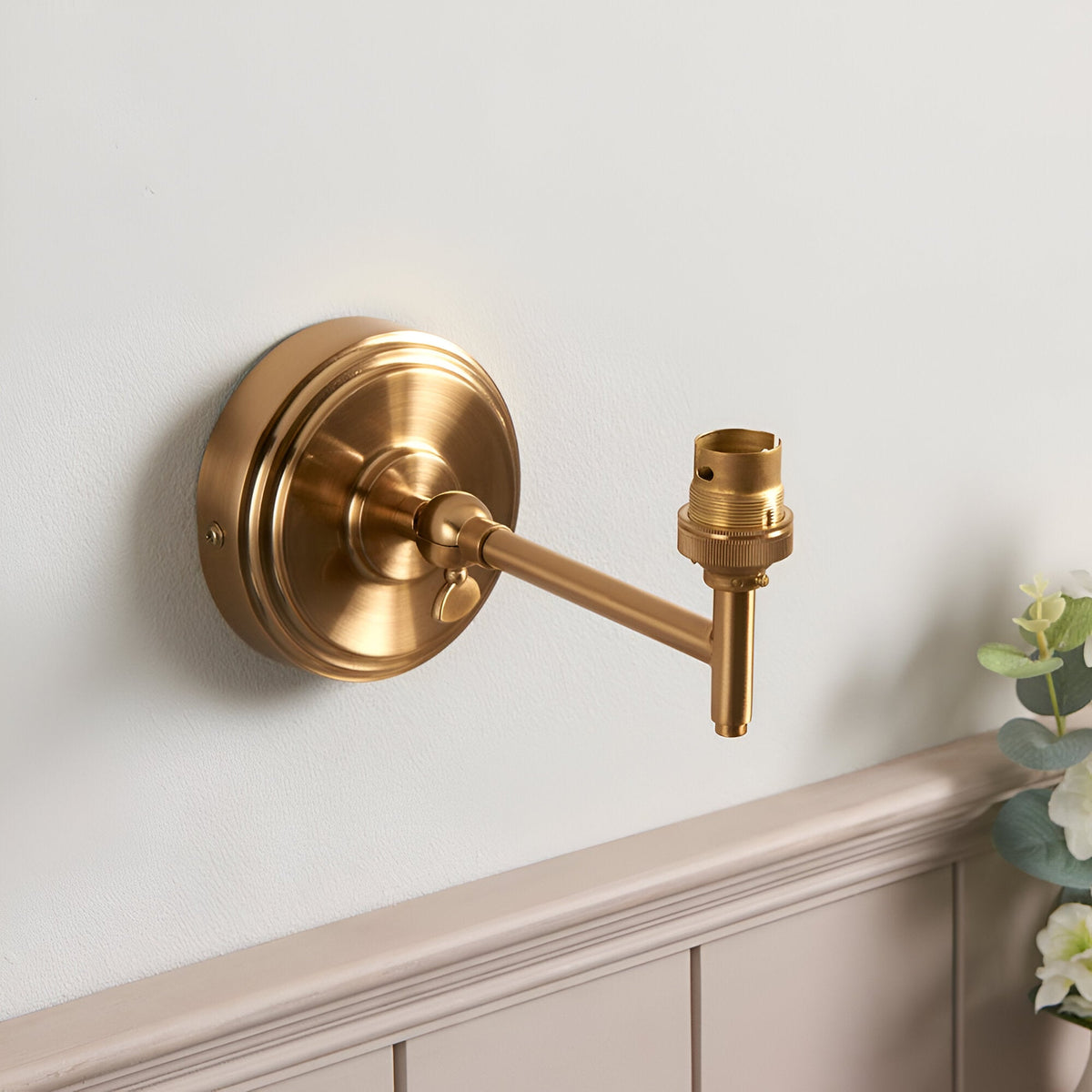 Endon Cliffwood wall light in brushed aged brass with a stepped round backplate, adjustable knuckle, linear arm, and B22 lampholder, mounted above panelling.