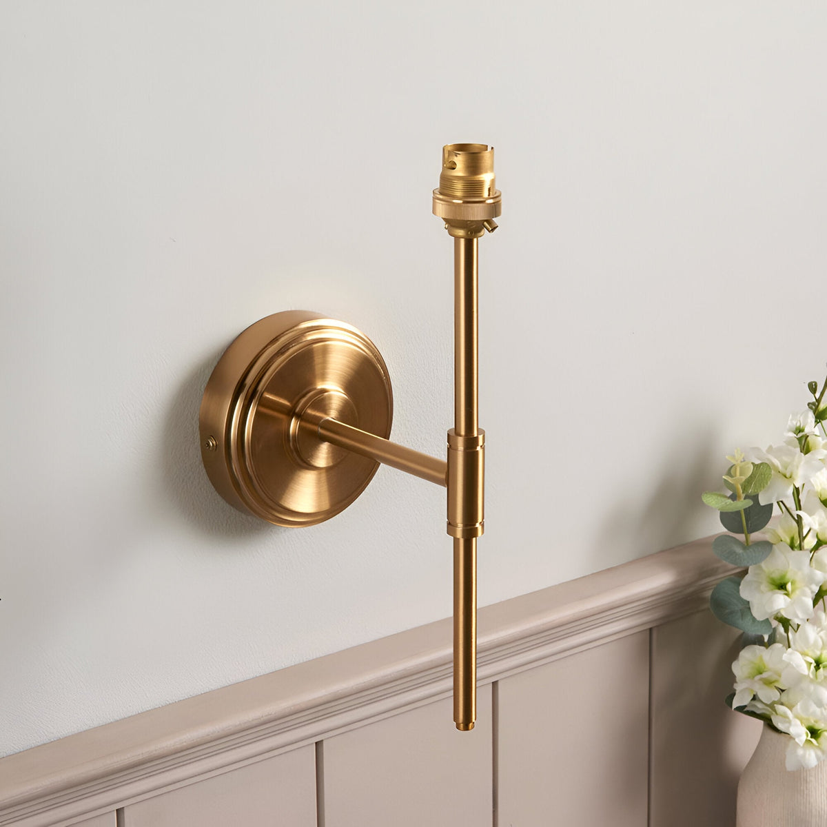 Endon Cliffworth wall light in brushed aged brass with stepped round backplate, T-bar arm and B22 lampholder, mounted above panelled wainscoting.
