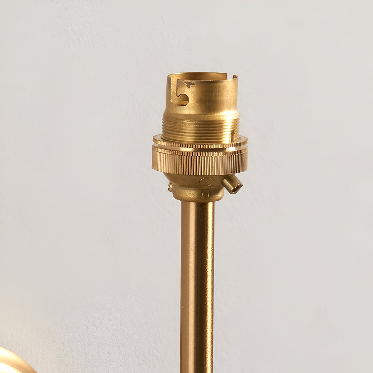 Close-up of the Endon Cliffworth wall light's brushed aged brass B22 lampholder and slim stem against a pale wall.