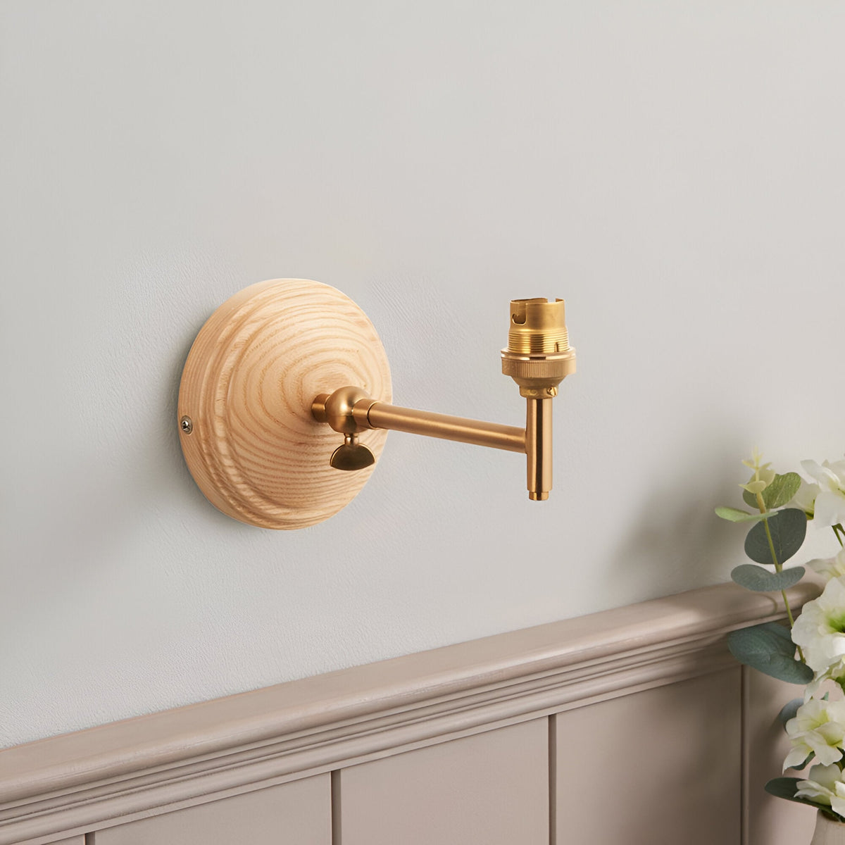 Endon Danemere wall light in natural ash with brushed aged brass adjustable arm and B22 lampholder, mounted on a light grey wall above panelling.