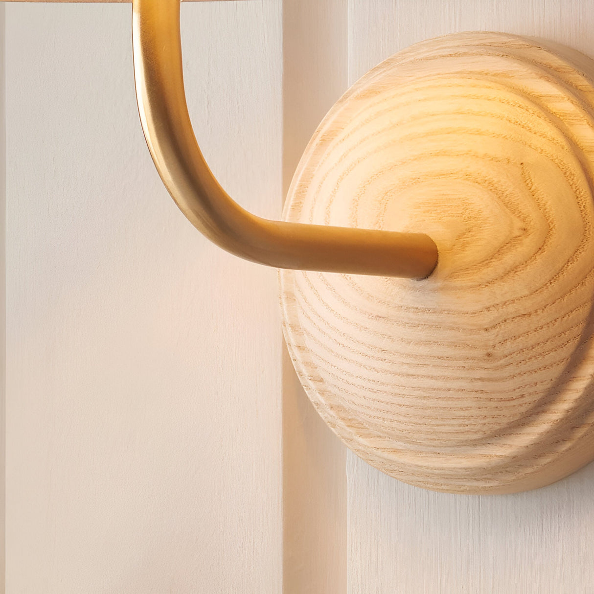 Close-up of Endon Daneleigh wall light showing the curved brushed aged brass arm meeting the round natural ash wood back plate with visible grain rings.