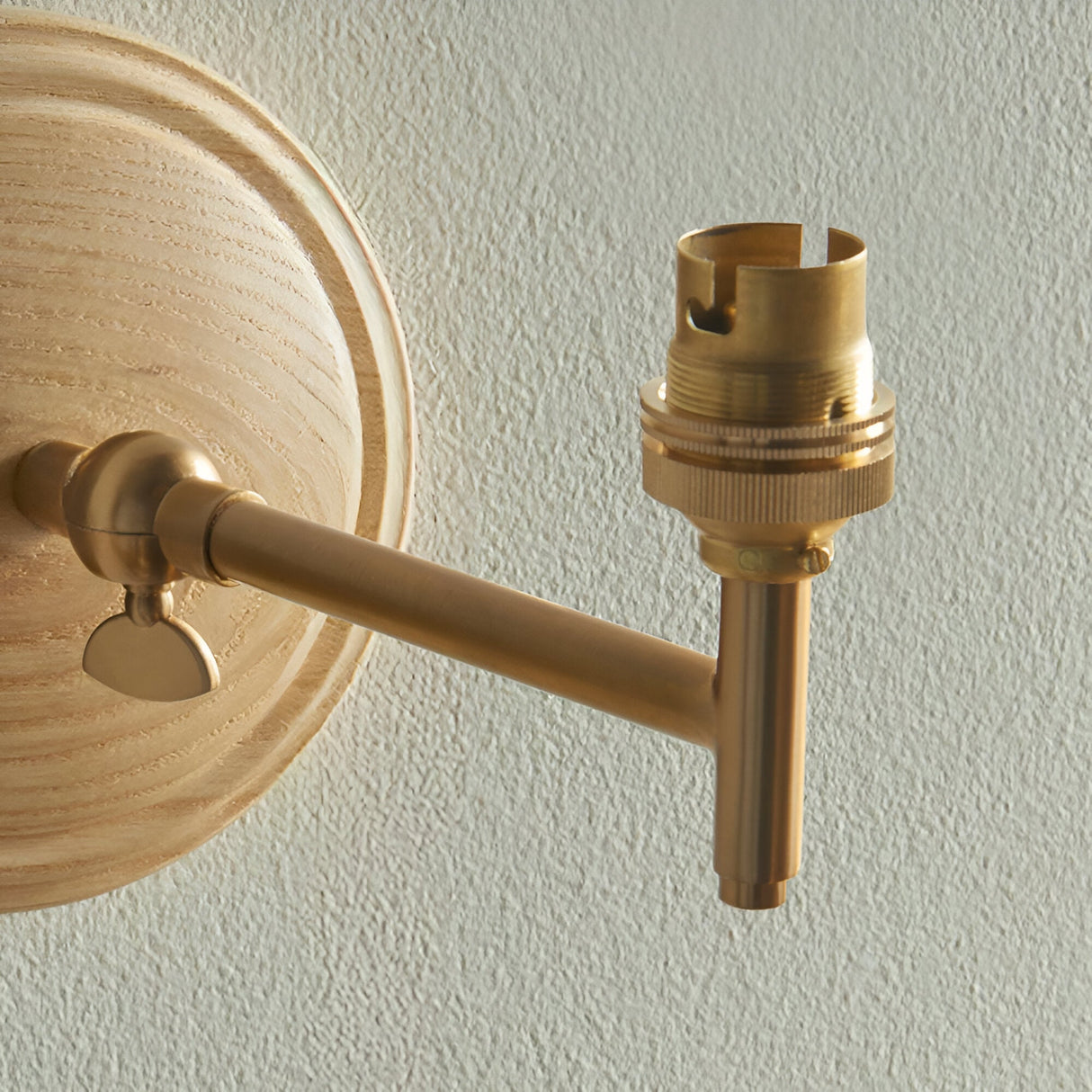 Close-up of the Endon Daneley wall light showing its brushed aged brass arm, adjustable knuckle, B22 holder, and natural ash wood back plate.