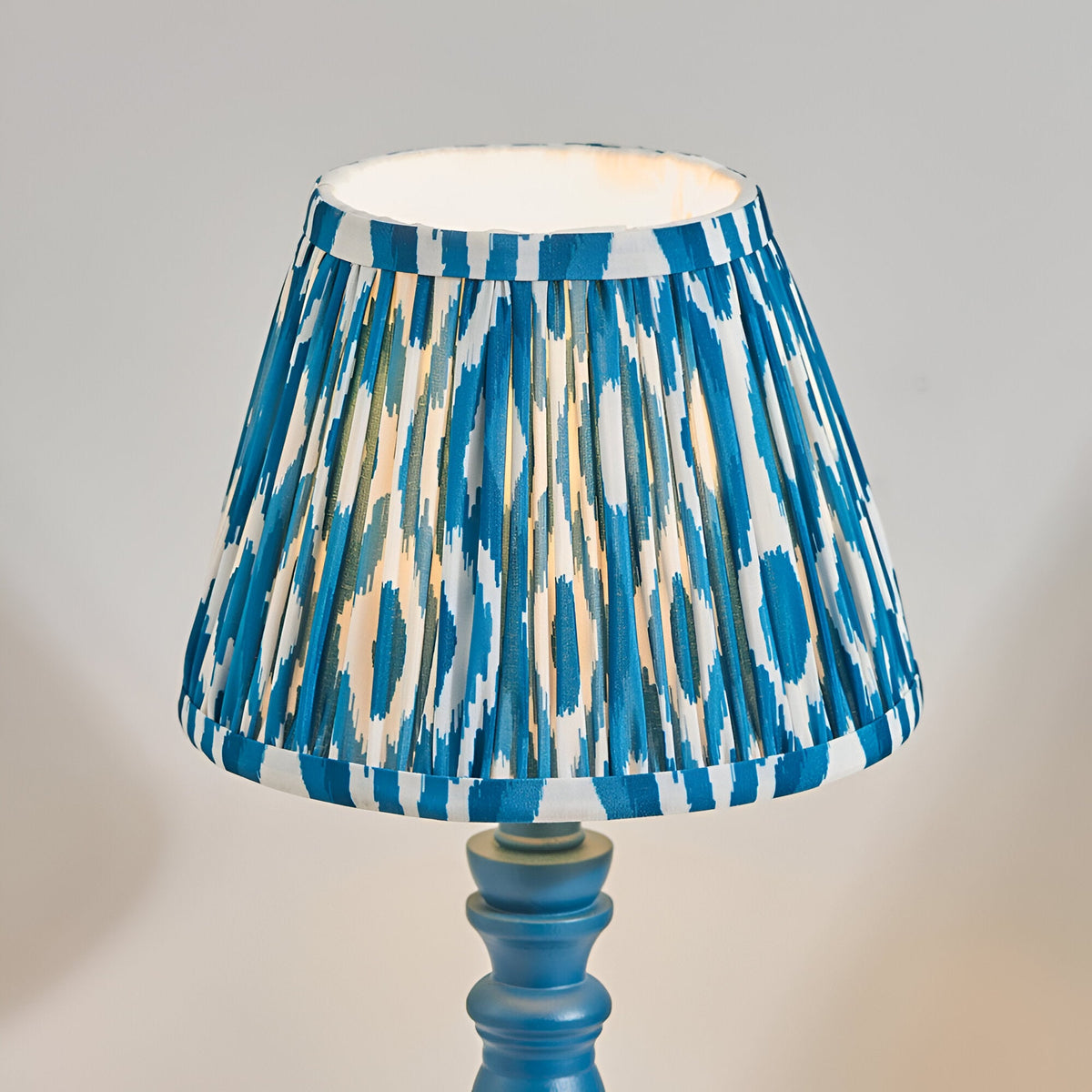 Endon Aldworth Ikat table lamp with a pleated blue and white ikat faux silk shade on a turned marlin blue spindle base, shown lit against a pale background.