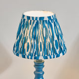 Endon Aldworth Ikat table lamp with a pleated blue and white ikat faux silk shade on a turned marlin blue spindle base, shown lit against a pale background.