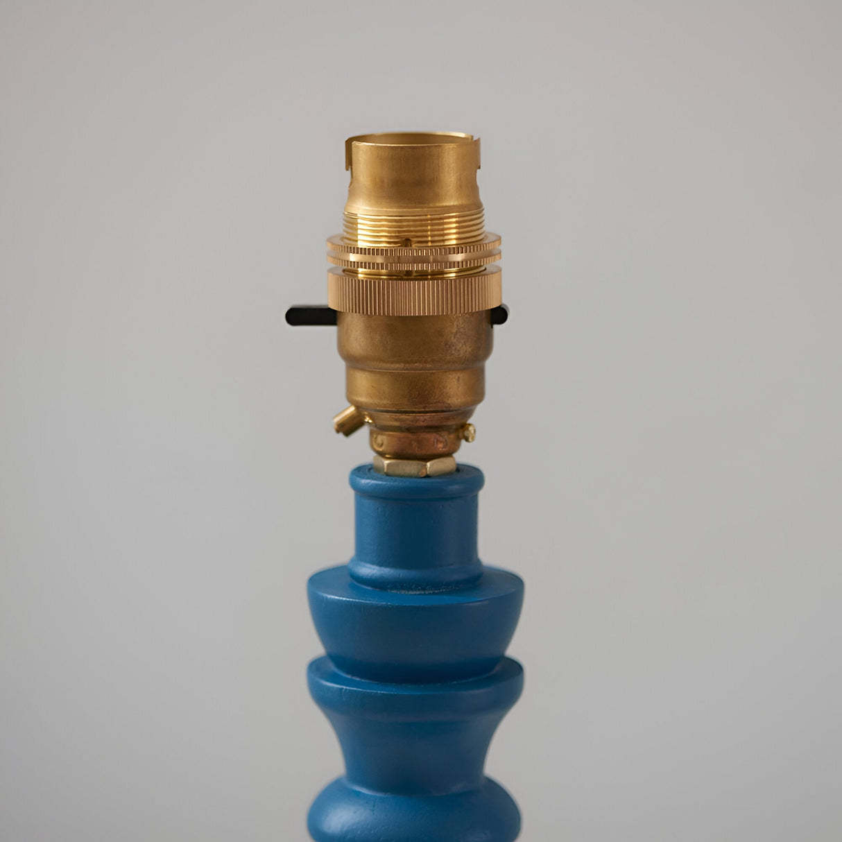 Close-up of the Endon Aldworth Ikat table lamp's brass B22 switched lampholder atop the turned marlin blue wooden spindle base.