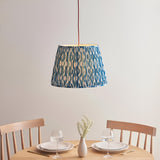 Endon Brackmont Ikat pendant light with pleated blue faux silk tapered shade and red fabric cable, hung above a wooden dining table set for two.