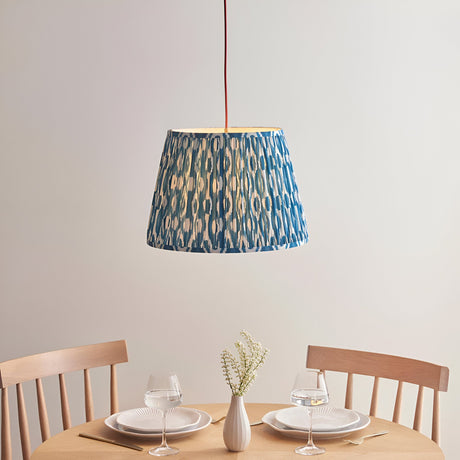 Endon Brackmont Ikat pendant light with pleated blue faux silk tapered shade and red fabric cable, hung above a wooden dining table set for two.