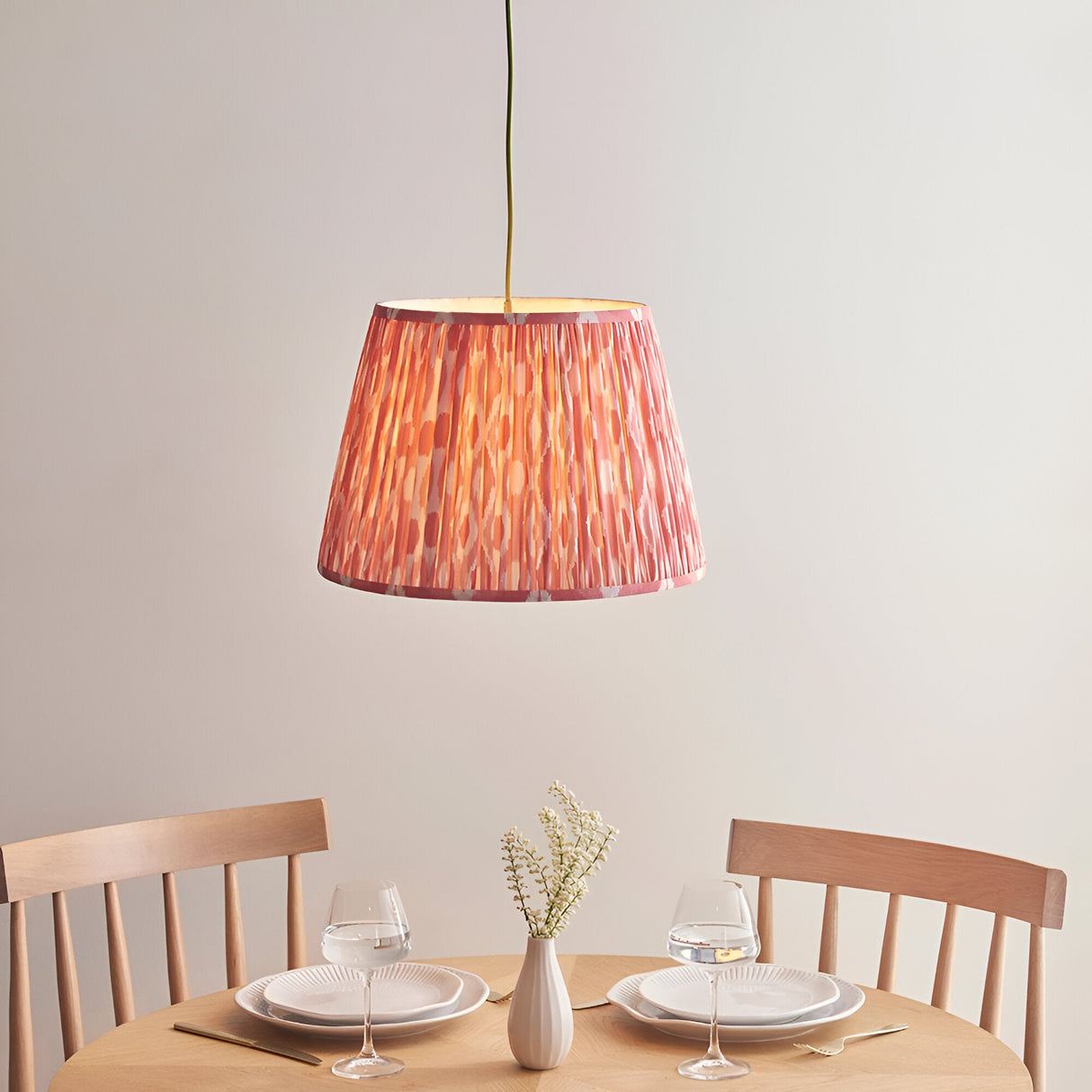 Endon Brackmont Ikat Coral pendant with handmade pleated faux silk shade and green braided cable, hung above a wooden dining table set for two.