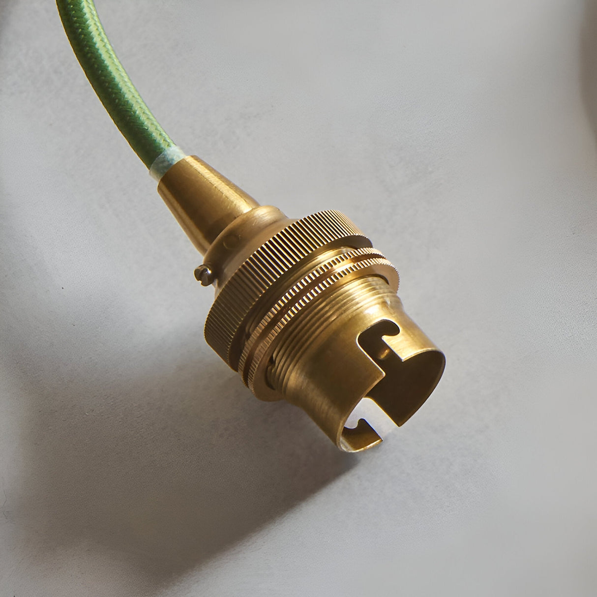 Close-up of the Endon Brackmont pendant's brushed aged brass B22 lampholder and green braided fabric cable against a light neutral background.