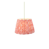 Endon Brackmont pendant light with handmade pleated tapered fabric shade in coral pink Ikat print, brass fitting and green braided cable, on white.