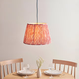 Endon Brackmont Ikat pendant with coral pink pleated faux silk tapered shade on a blue fabric cable, hanging above a wooden dining table set for two.