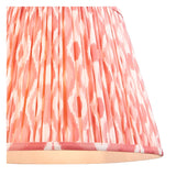 Endon Brackmont Ikat pendant shade in coral pink faux silk with handmade pleated taper and taped edge detailing, shown lit from within.