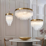 Endon Aldfield pendant lights in brushed brass with tiered clear glass rods, shown in three sizes above a round marble dining table.