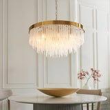 Aldfield 9 Light Pendant in brushed brass with tiered clear glass rods, hung above a marble dining table in a light-panelled room.
