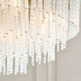 Aldfield nine-light pendant, close-up of twisted clear glass rods cascading from a brushed antique brass frame, lit against a plain light background.