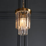 Endon Bevstead small single pendant with two-tier clear lozenge glass drops on a brushed aged brass frame and chain, lit against a dark panelled wall.