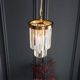 Endon Bevstead small single pendant with tiered clear lozenge glass drops on a brushed aged brass frame, hung against a dark panelled wall.