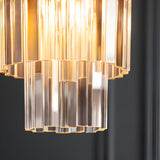 Close-up of Endon Bevstead pendant showing tiered clear lozenge glass drops on a brushed aged brass frame, lit against a dark grey wall.