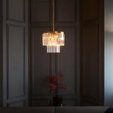 Bevstead 4-light pendant in brass with tiered clear glass drops, hanging lit in a dark panelled room above a small side table.