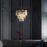 Endon Bevstead 7 light pendant in brushed brass with tiered clear crystal drops, hung against a dark panelled wall above a grey sofa.
