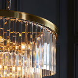 Close-up of the Endon Bevstead 7 light pendant showing tiered clear cut lozenge glass drops and a brushed brass band against a dark wall.