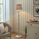 Endon Bevbury floor lamp with turned white spindle base and grey zigzag pleated shade, beside a wicker chair and cream sideboard in a living room.