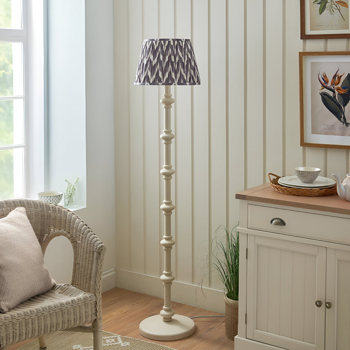 Endon Bevbury floor lamp with turned white spindle base and grey zigzag pleated shade, beside a wicker chair and cream sideboard in a bright living room.