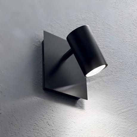 The Radiatrix Wall Light - Black is a sleek, modern lighting fixture with a cylindrical shape. It features an adjustable diffuser, casting bright light onto a textured grey wall.