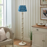 Endon Bevbury Ikat floor lamp with turned white spindle base and blue pleated Ikat patterned shade, styled in a neutral living room beside a wicker chair.