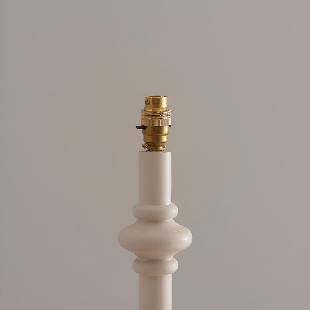 Close-up of the Endon Bevbury floor lamp's turned white wooden spindle base and switched brass B22 lamp holder against a neutral background.