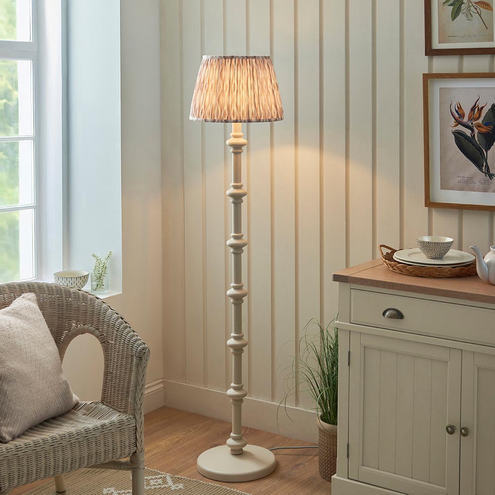 Bevbury Ikat Floor Lamp with turned wooden white base and pleated grey patterned fabric shade, shown in a living room beside a sideboard.