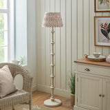 Bevbury Ikat Floor Lamp with turned wooden spindle base in cream, topped with a pleated patterned fabric shade, shown in a living room setting.