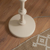Close-up of the Bevbury Ikat Floor Lamp's turned wooden base in a matte natural finish, shown on wood flooring beside a patterned rug.