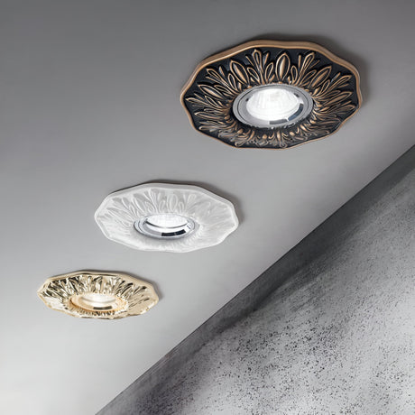 Three Olivia Recessed Downlights in ornate decorative frames, including antique brass, are mounted on a textured ceiling. The frames come in dark brown, white, and gold, each showcasing an intricate floral design that adds an elegant touch to the space; their recessed downlight style seamlessly enhances the ambiance.