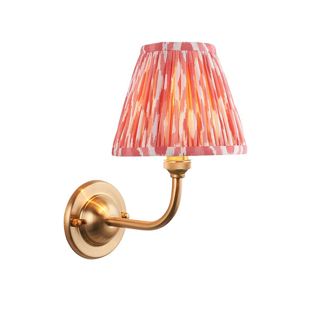 Endon Brackdale Ikat wall light with a brushed aged brass curved arm and round backplate, topped by a pleated coral pink ikat-print fabric shade.