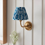 Endon Brackdale Ikat wall light with brushed aged brass curved arm and pleated marlin blue ikat faux silk shade, mounted on a white panelled wall.