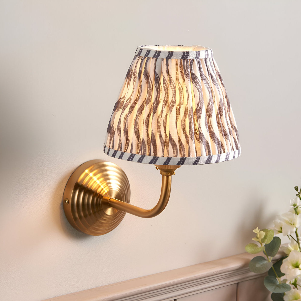 Endon Castgrove Ripple wall light with brushed aged brass stepped backplate, curved arm and pleated grey faux linen ripple-print tapered shade.