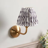 Endon Castgrove Ripple wall light with a stepped brushed aged brass backplate, curved arm, and tapered pleated pearl grey faux linen shade with ripple print.