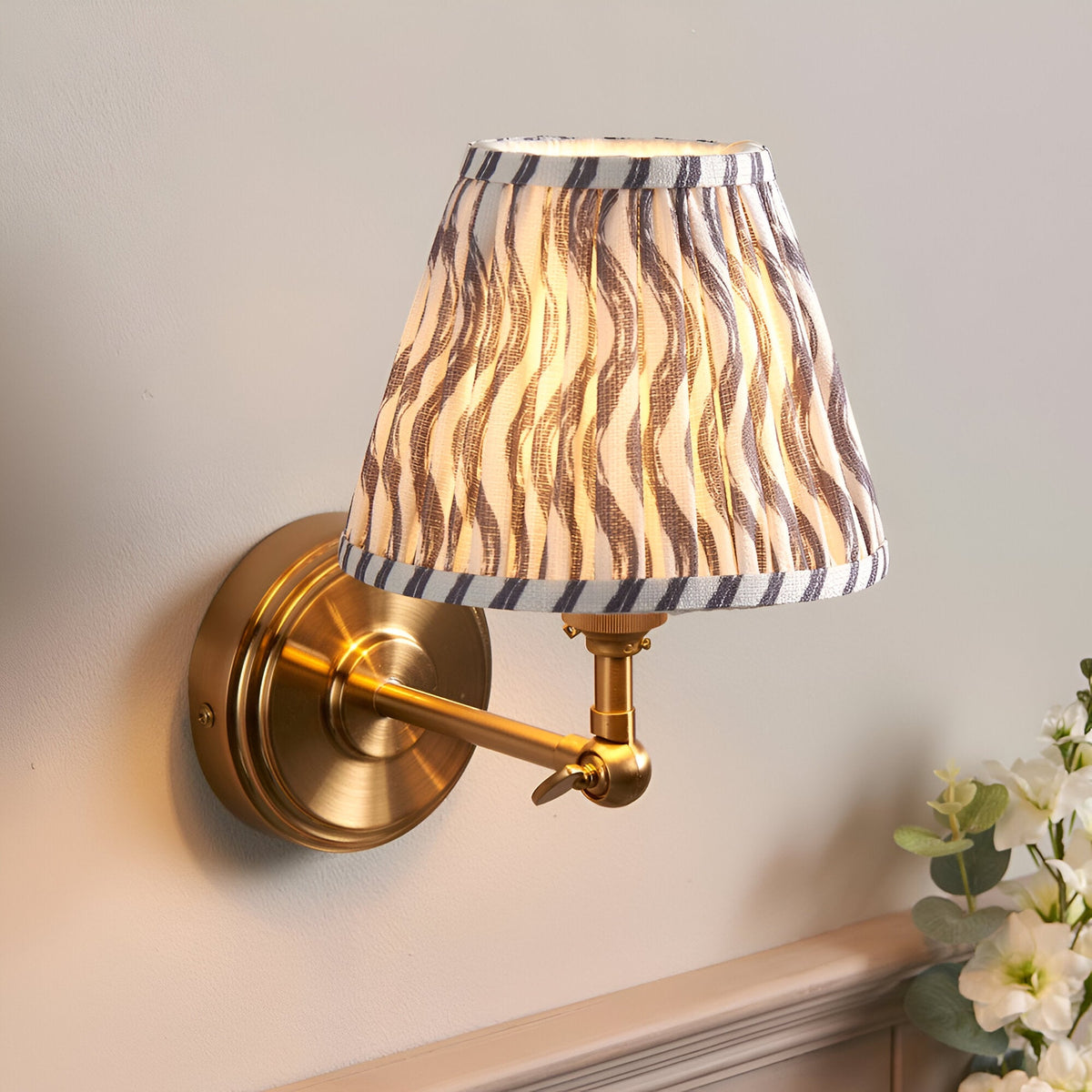 Endon Corven wall light with brushed brass stepped base, adjustable arm, and tapered pleated shade in grey Ripple print on faux linen.
