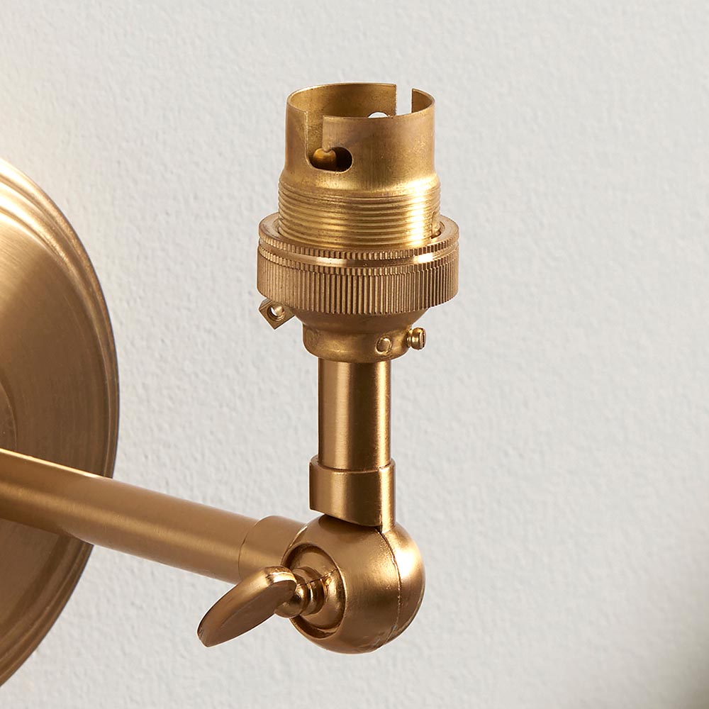 Close-up of the Corven wall light's brass B22 lamp holder and adjustable knuckle joint on a linear arm, against a plain light background.