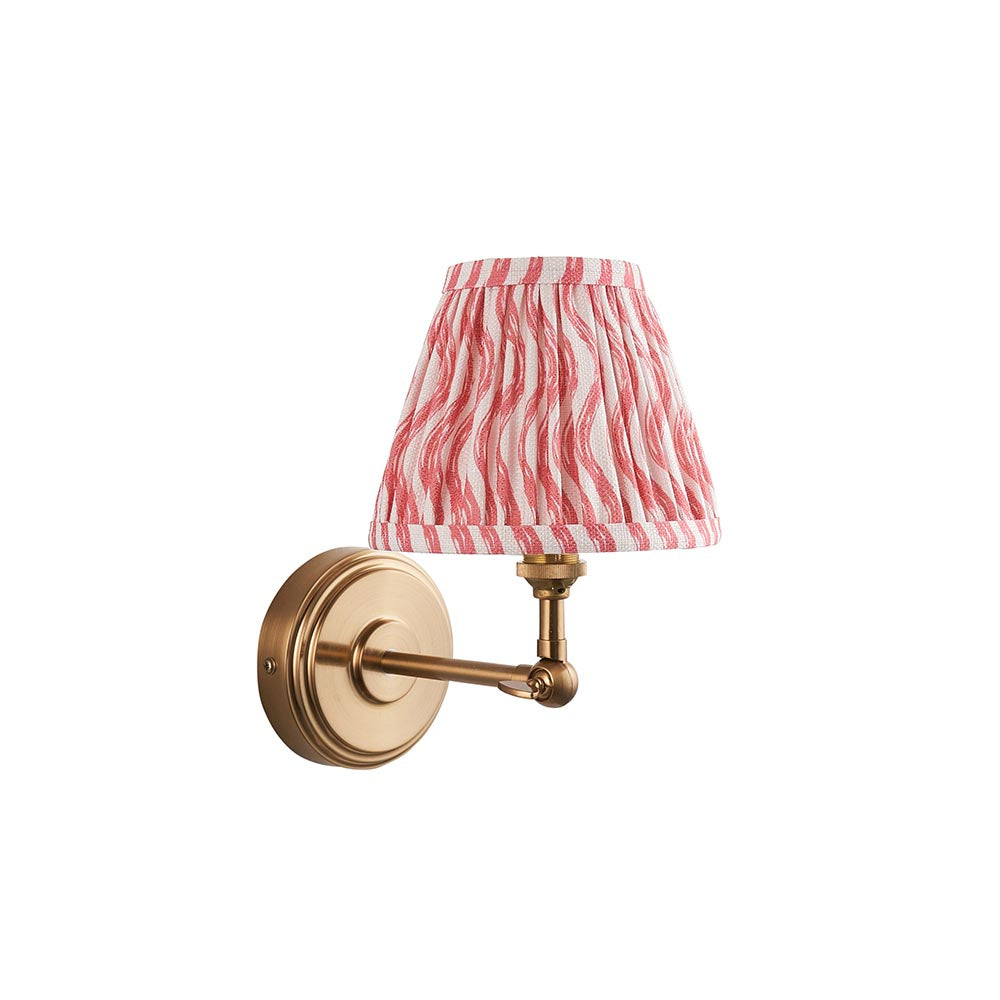 Corven wall light in brushed brass with an adjustable knuckle arm and pleated pink and white ripple-print fabric shade, shown on a plain white background.