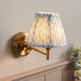 Endon Cliffwood Leaf wall light in brushed aged brass with an adjustable arm and pleated blue leaf-print fabric shade, mounted on a pale wall.