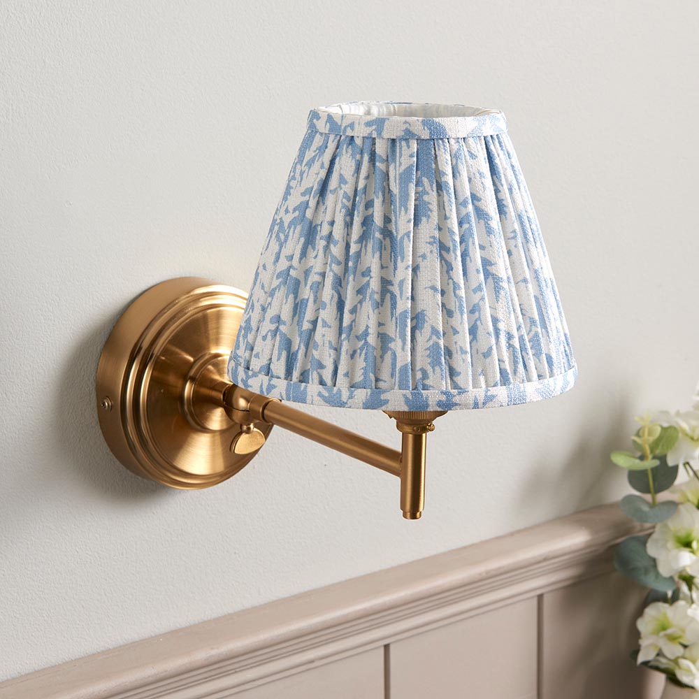 Endon Cliffwood Leaf wall light with brushed aged brass stepped base, adjustable arm, and blue leaf-print pleated faux linen shade on a pale wall.