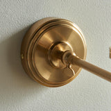 Close-up of the Endon Cliffwood wall light's brushed aged brass backplate and adjustable knuckle joining the linear arm, mounted on a pale wall.