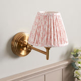 Cliffwood Leaf Wall Light in brushed brass with an adjustable knuckle arm and pleated pink leaf-print fabric shade, shown mounted on a light wall.