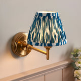 Cliffwood Ikat wall light with brushed brass adjustable arm and swing-arm bracket, pleated blue and white Ikat-print fabric shade, mounted on a light grey wall.