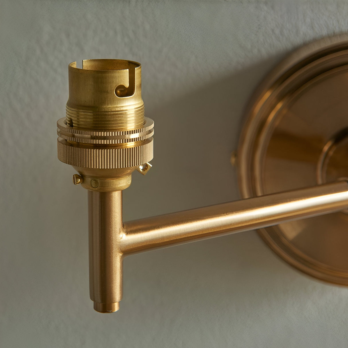Close-up of the Cliffwood wall light's brass B22 lamp holder and adjustable knuckle arm with circular wall backplate, shown against a plain light background.