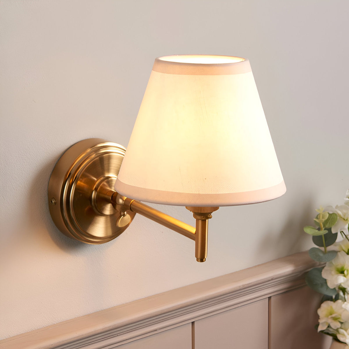 Endon Cliffwood Ivy wall light in brushed aged brass with adjustable arm and tapered vintage white fabric shade, mounted above panelled wainscoting.