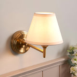 Endon Cliffwood Ivy wall light in brushed aged brass with adjustable arm and tapered vintage white fabric shade, mounted above panelled wainscoting.