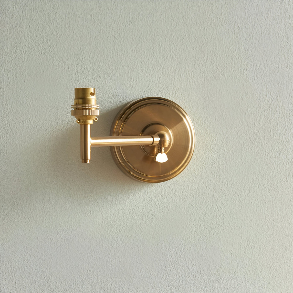 Endon Cliffwood Ivy wall light in brushed aged brass with adjustable knuckle arm and B22 lamp holder, shown without shade on a pale wall.